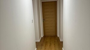 A narrow hallway with white walls and wooden flooring, leading to a wooden door at the end. - Mansfield City Centre - AvanteFirst (Mansfield)