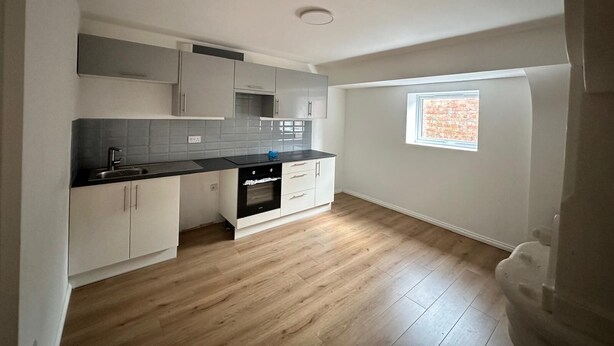 A modern kitchen with grey cabinets, a black countertop, and a built-in oven. - Mansfield City Centre - AvanteFirst (Mansfield)