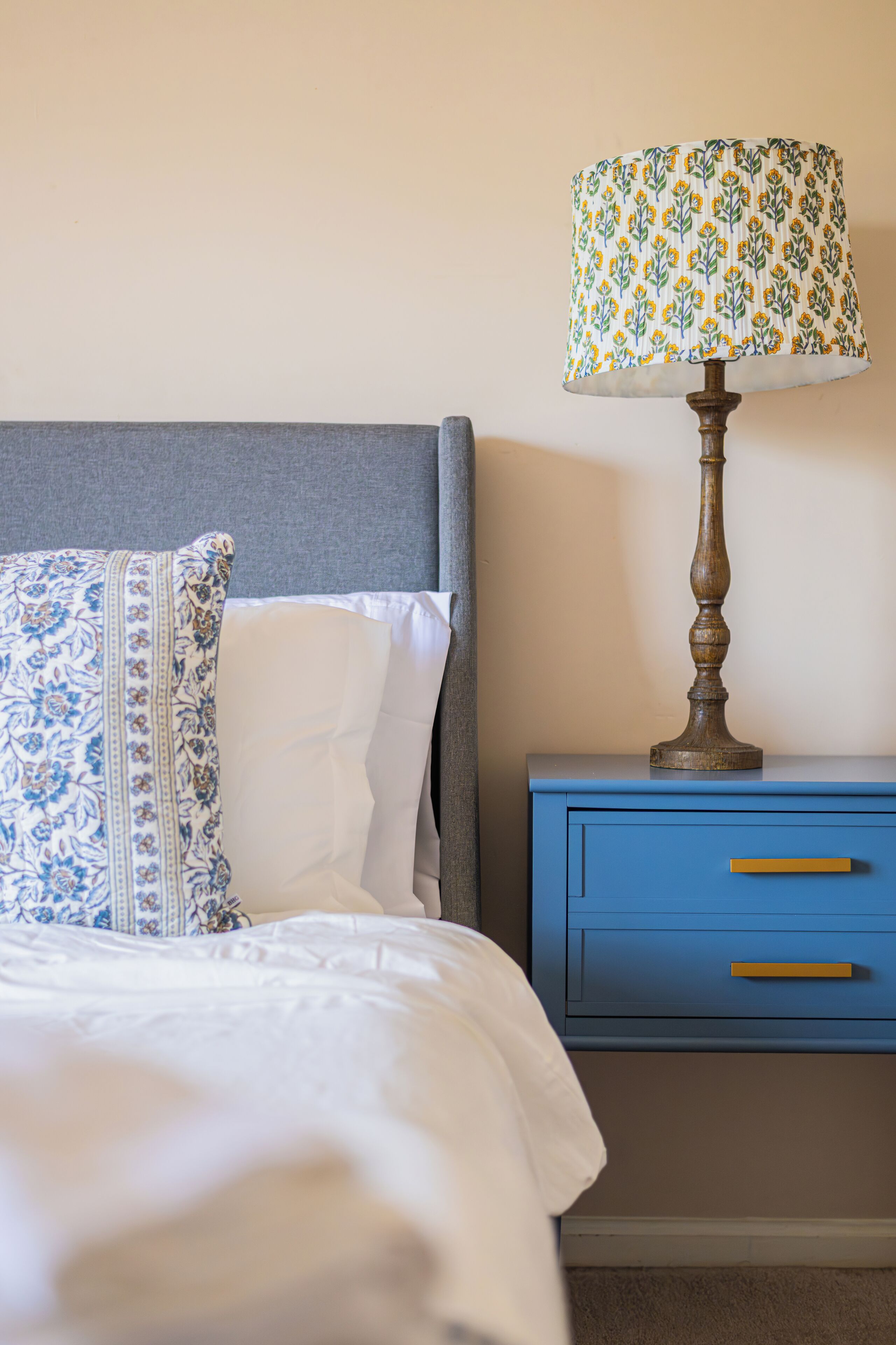 A neatly made bed with a patterned pillow and a blue bedside table with a lamp.
