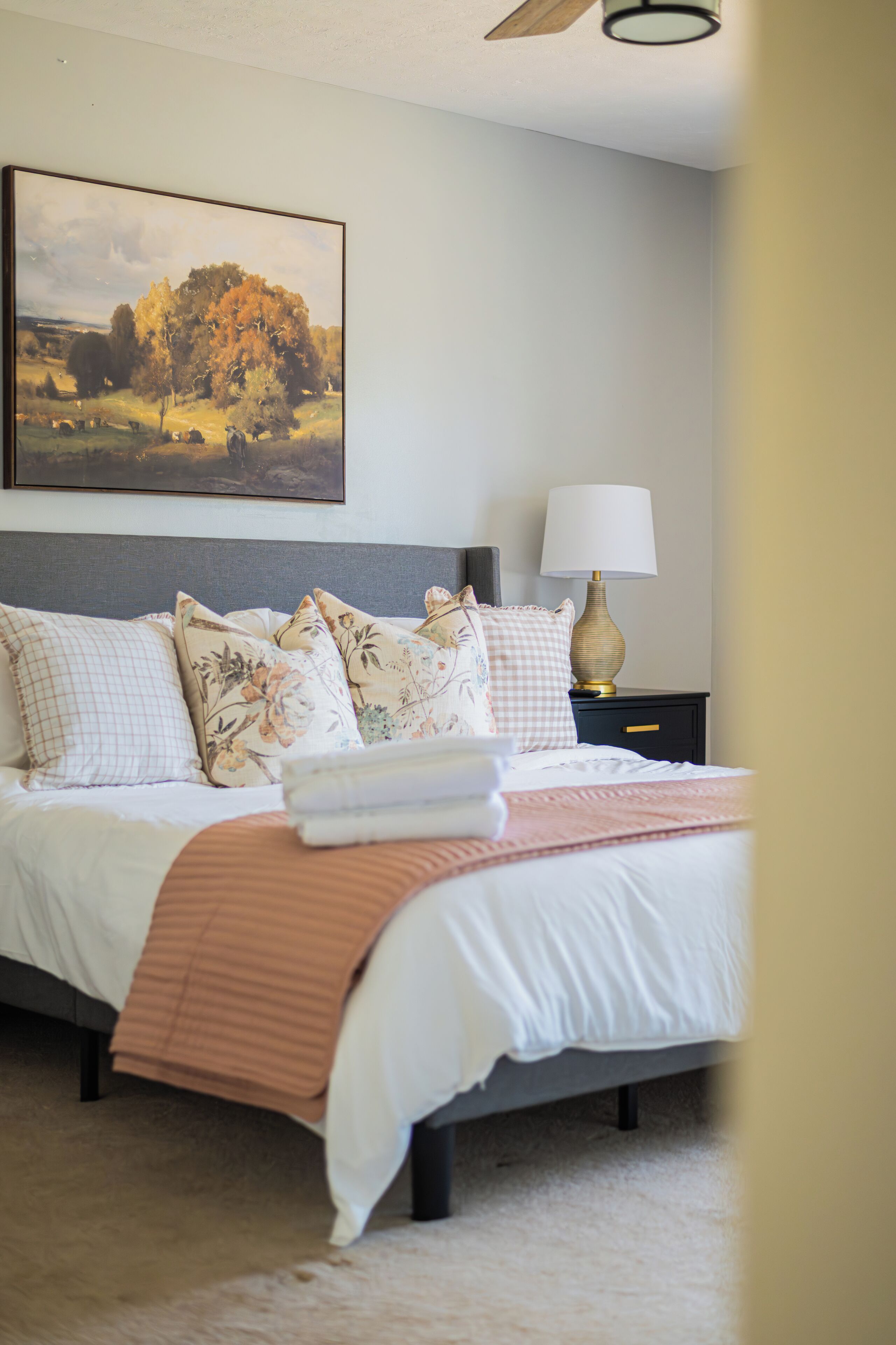 A bedroom with a bed, pillows, a bedside table with a lamp, and a painting on the wall.