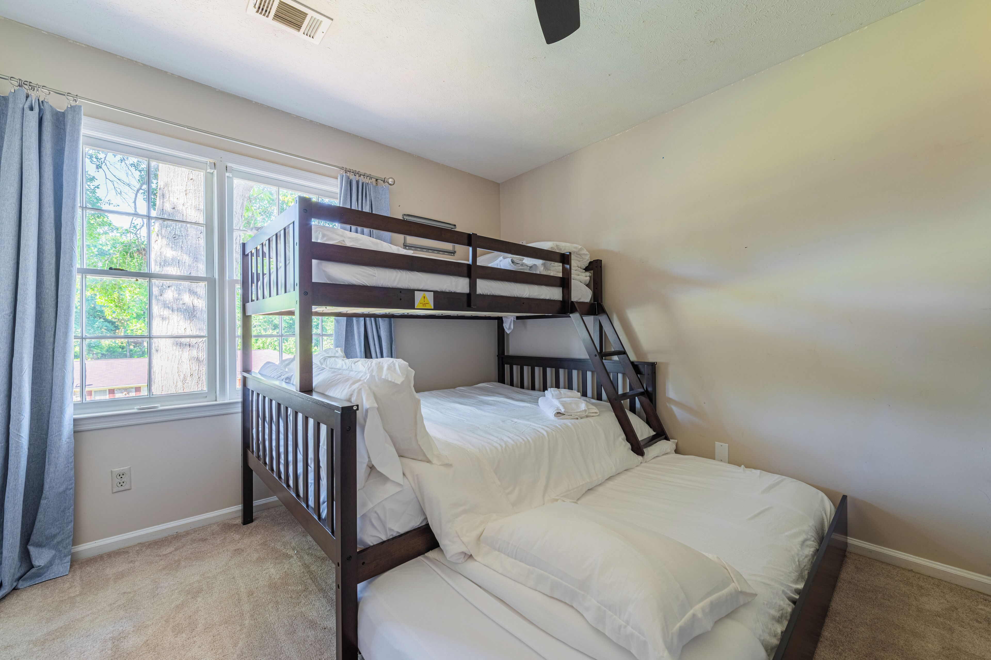 Dormitorio con literas, ventana, cortinas y ventilador de techo.