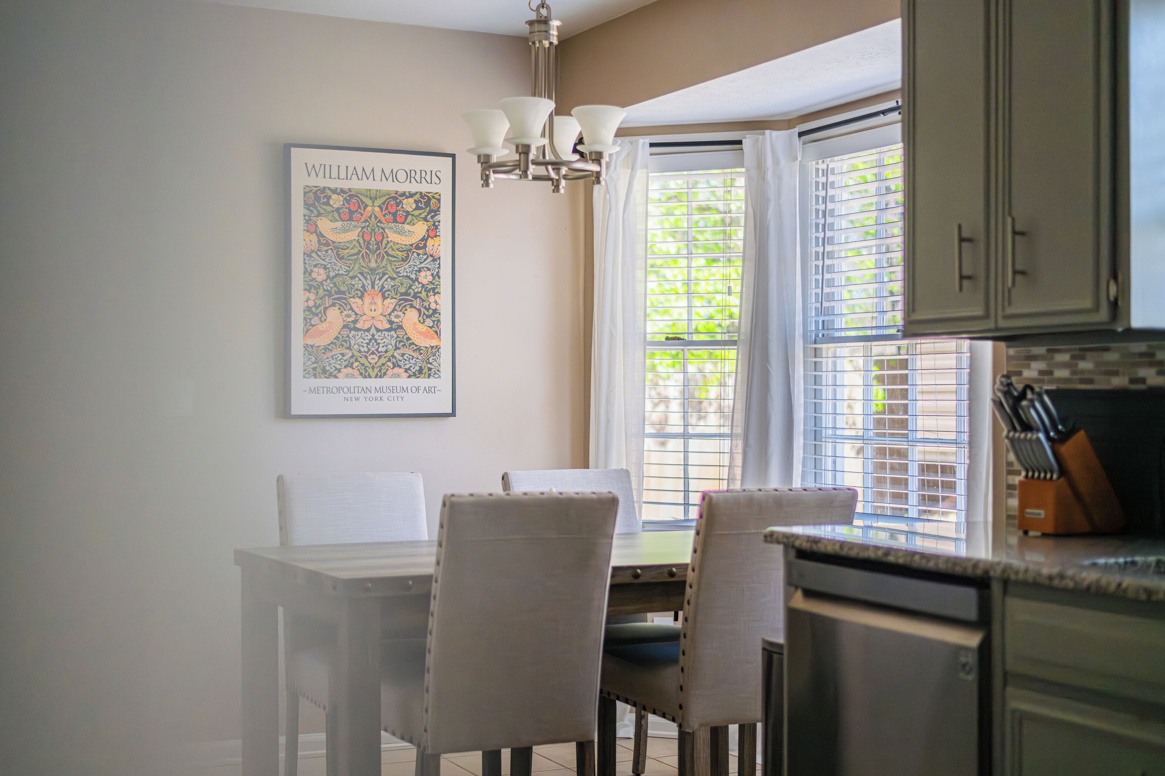 A dining area with a table and chairs, a chandelier, and a window with blinds.