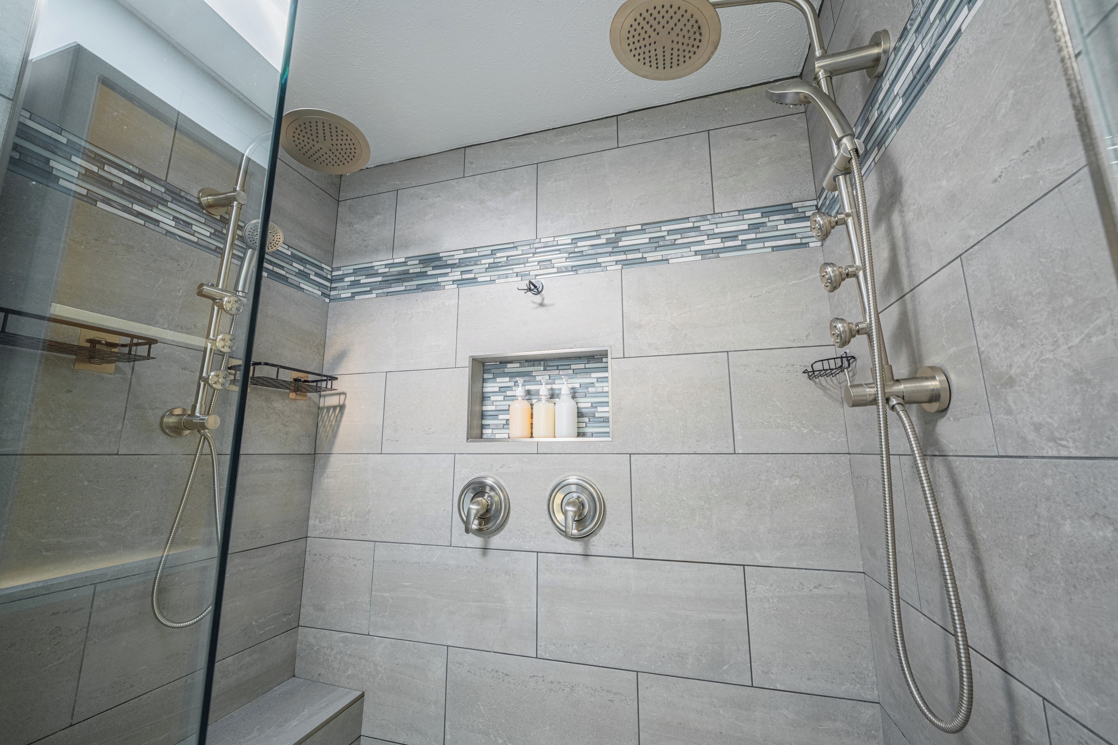 Eine moderne Dusche mit mehreren Brausen, einer Glasabtrennung und einem kleinen Fenster mit Toilettenartikeln.