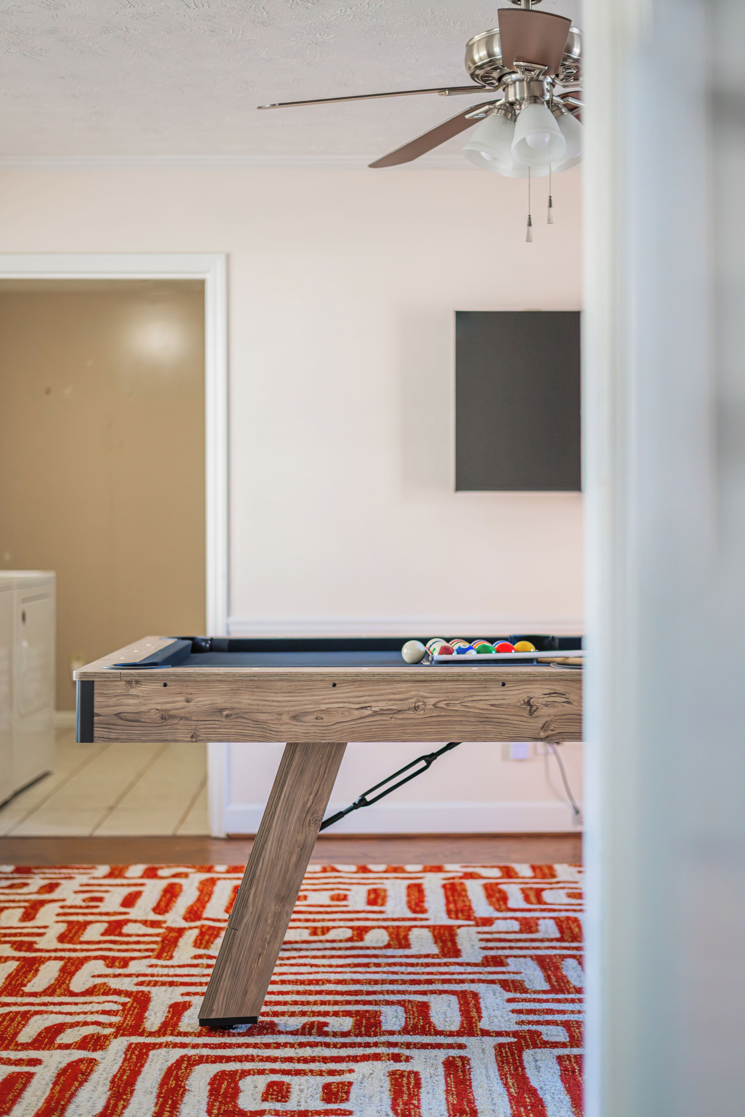 A pool table in a room with a patterned carpet, a ceiling fan, and a framed picture on the wall.
