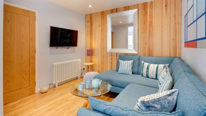 Een moderne woonkamer met een blauwe bank, houten paneelwanden, een flatscreen televisie en een glazen salontafel.