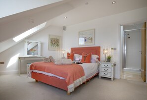 Ein Schlafzimmer mit geneigter Decke, einem Bett mit weißer und orangefarbener Bettdecke, einem Nachttisch mit Lampe und einem gerahmten Bild an der Wand.