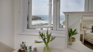 Una habitación con vistas al océano, un aparador blanco, un jarrón con flores y una cafetera.