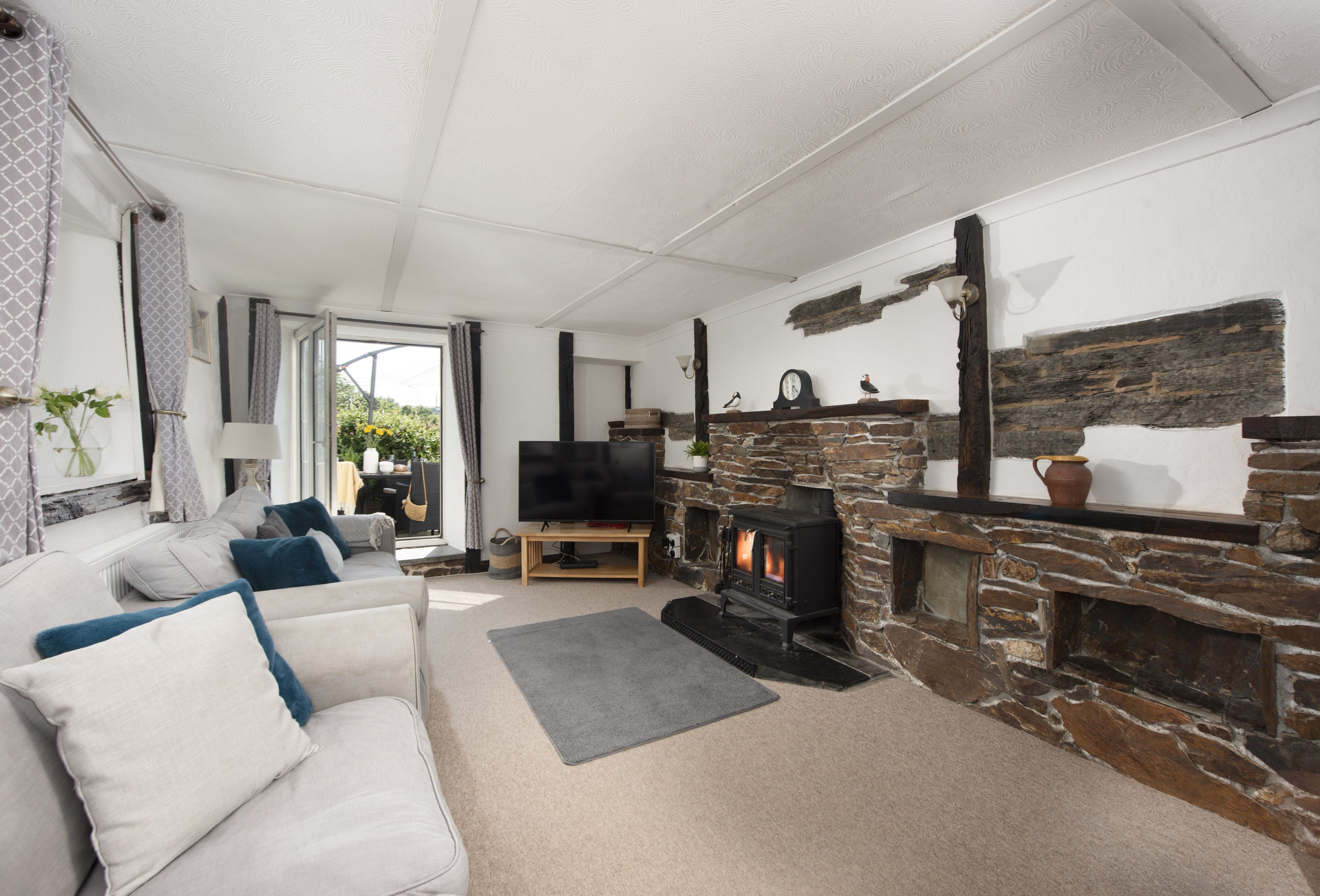 A cozy living room with a stone fireplace, a sofa with cushions, a television, and a view through a glass door.