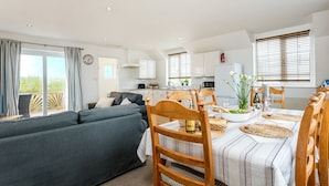 A modern living space with a dining area, a sofa, and a kitchen in the background. - Arnold Cottage is a perfect hideaway for couples, families, or small groups looking to unwind (St. Merryn, Treyarnon Bay)