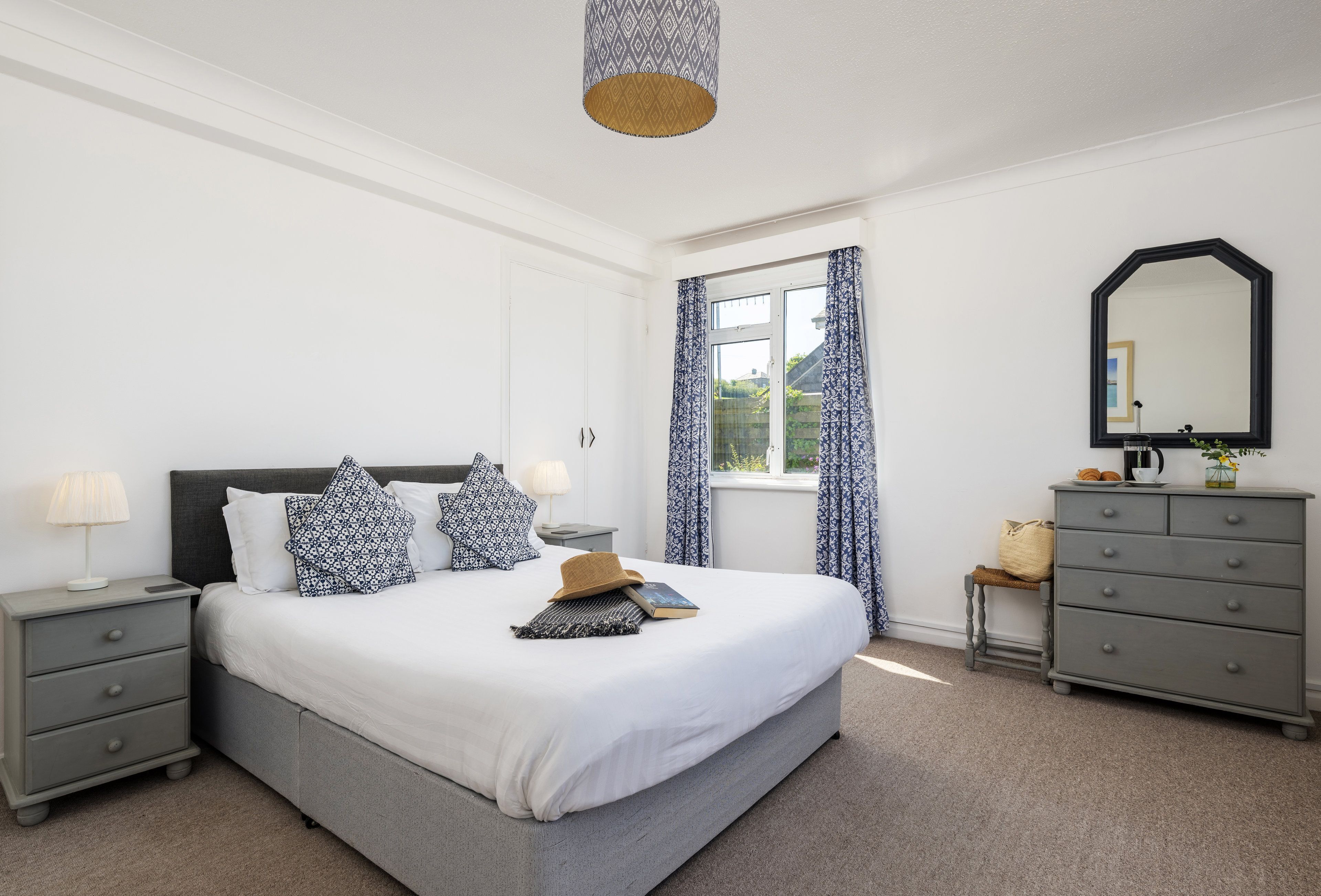 A neatly arranged bedroom with a bed, bedside tables, a dresser, and a window with curtains.