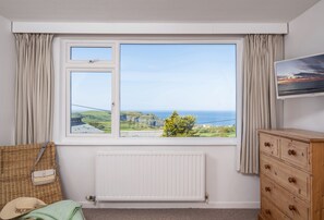 Una habitación con un ventanal grande, un radiador, un aparador de madera y una cesta de mimbre.