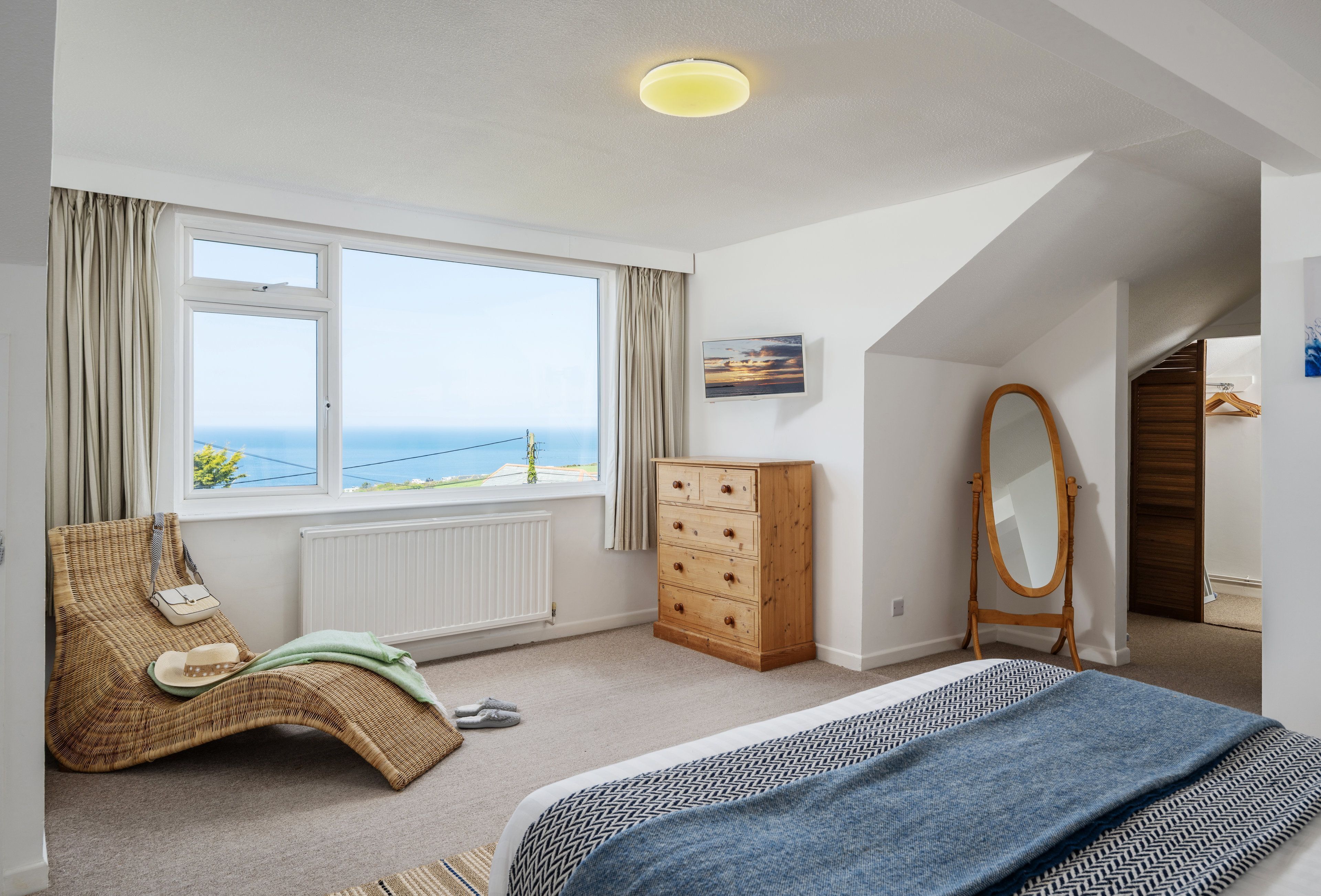 A bedroom with a large window, a wooden dresser, a mirror, and a bed.