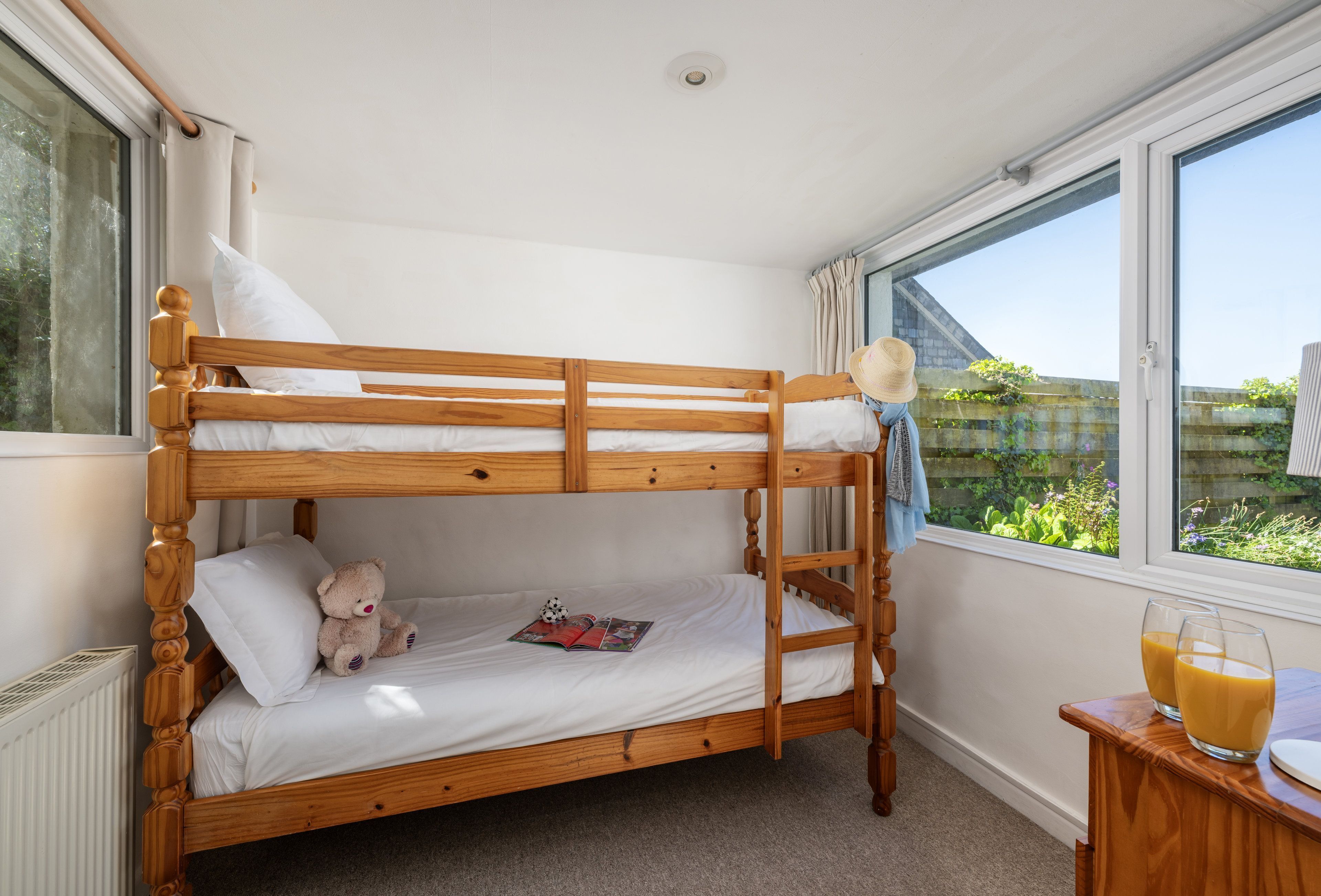 A bunk bed with a wooden frame, white bedding, a teddy bear, and a book on the lower bunk.
