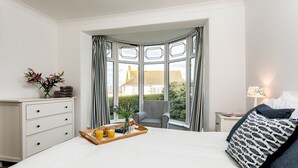 A hotel room with a bed, a chair, a nightstand, a window with curtains, and a tray with a drink and flowers. - Welcome to Bay View, a stunning five-bedroom dog-friendly holiday home (Port Isaac)