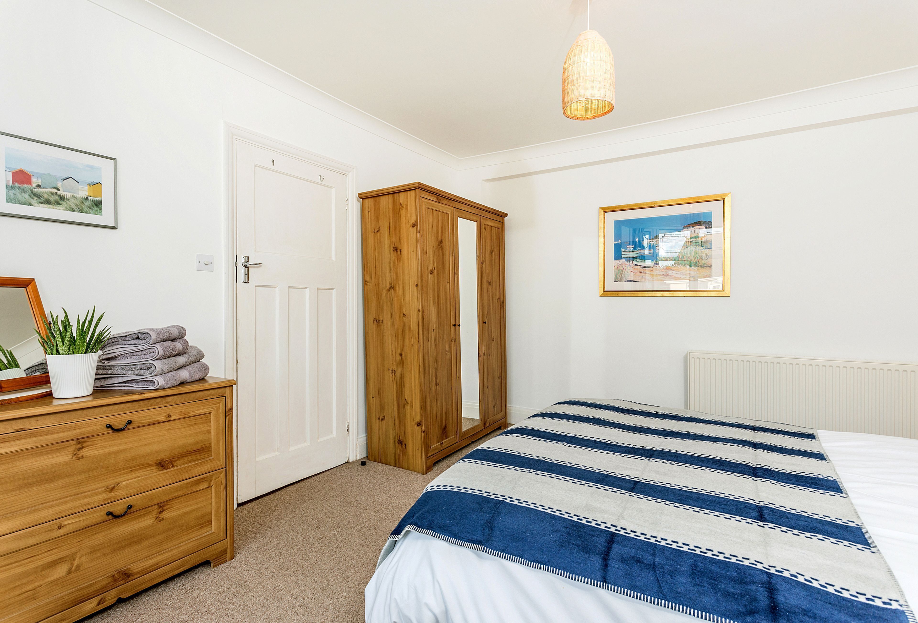 A bedroom with a bed, wooden wardrobe, dresser, and two framed pictures on the wall.