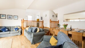 A spacious living room with grey sofas, a wooden staircase, and a dining area with wicker chairs and a table set for two. - Welcome to Bay View, a stunning five-bedroom dog-friendly holiday home (Port Isaac)