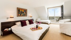 Une chambre d’hôtel moderne dotée d’un grand lit, d’un lit plus petit, d’un canapé et d’un balcon avec vue.