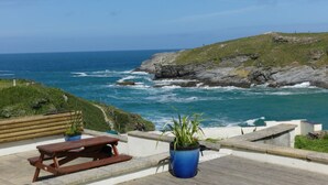 Une terrasse en bord de mer, avec un banc en bois, un pot de fleurs et une vue sur l’océan.