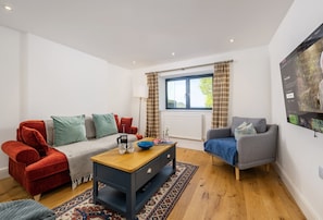 A modern living room with a sofa, armchair, coffee table, and a large window with curtains.
