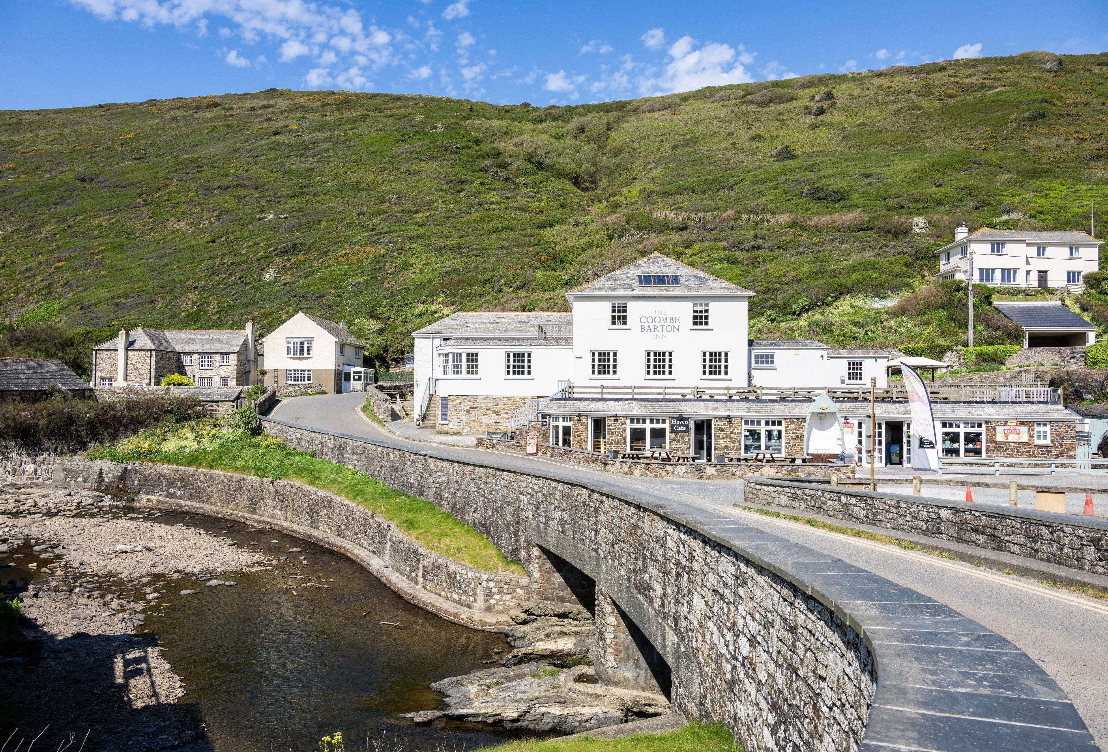 Une route côtière avec un pont de pierre menant à un bâtiment blanc portant l’inscription « The Coombe Barton Inn ».