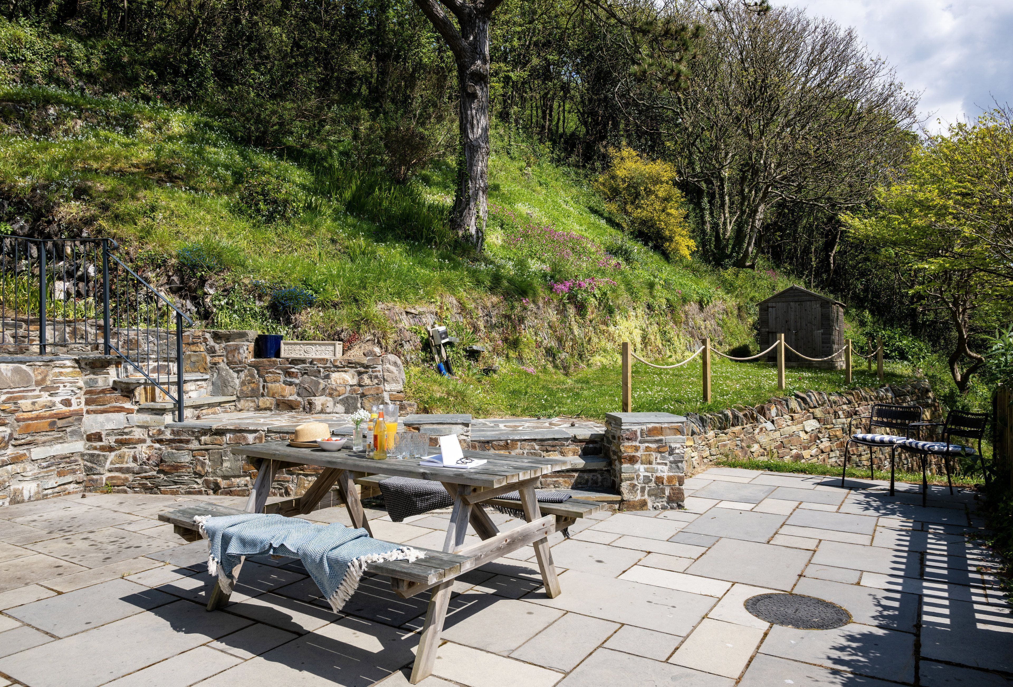 Un patio al aire libre con paredes de piedra, una mesa de madera y bancos.