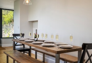 A dining table set with plates, glasses, and a bottle of wine, with a view of greenery outside.