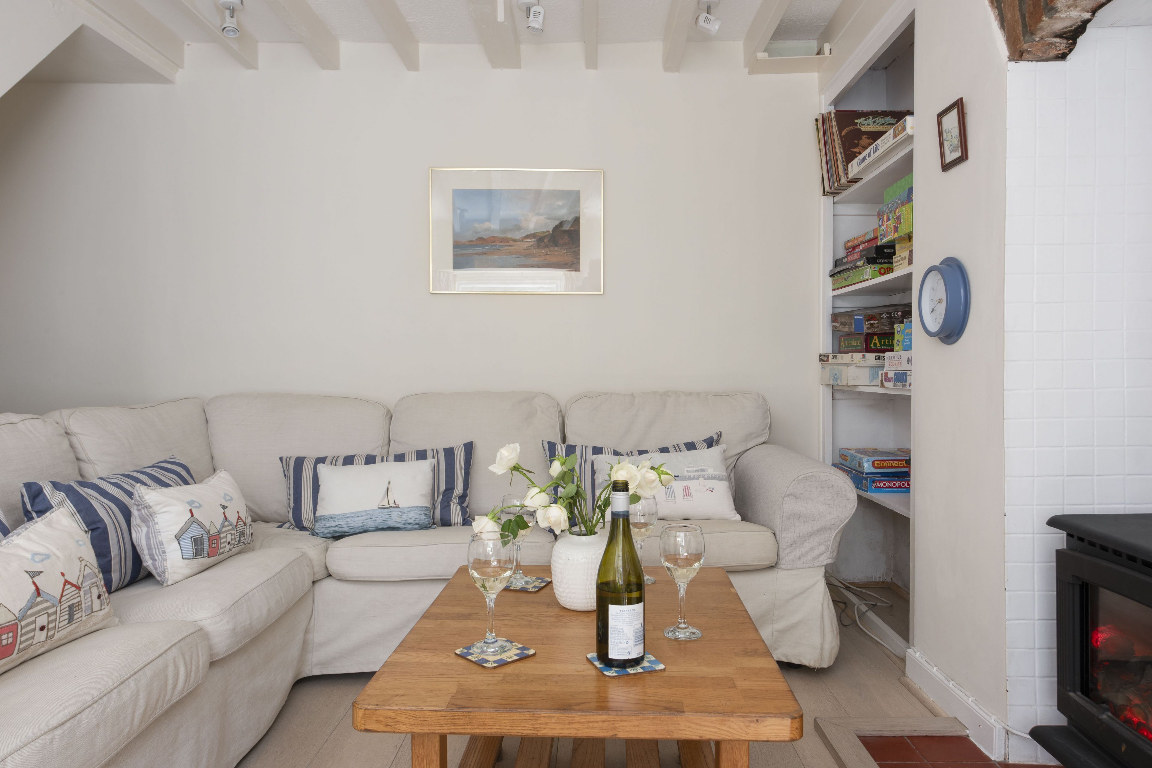 Una sala de estar con un sofá color beige, una mesa de centro de madera con una botella de vino y copas, y una estantería con diversos objetos.