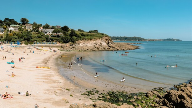 A beach with people, boats, and houses in the background.