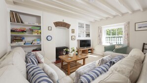 A living room with a sofa set, a wooden coffee table, a bookshelf with board games, a fireplace, and a television.