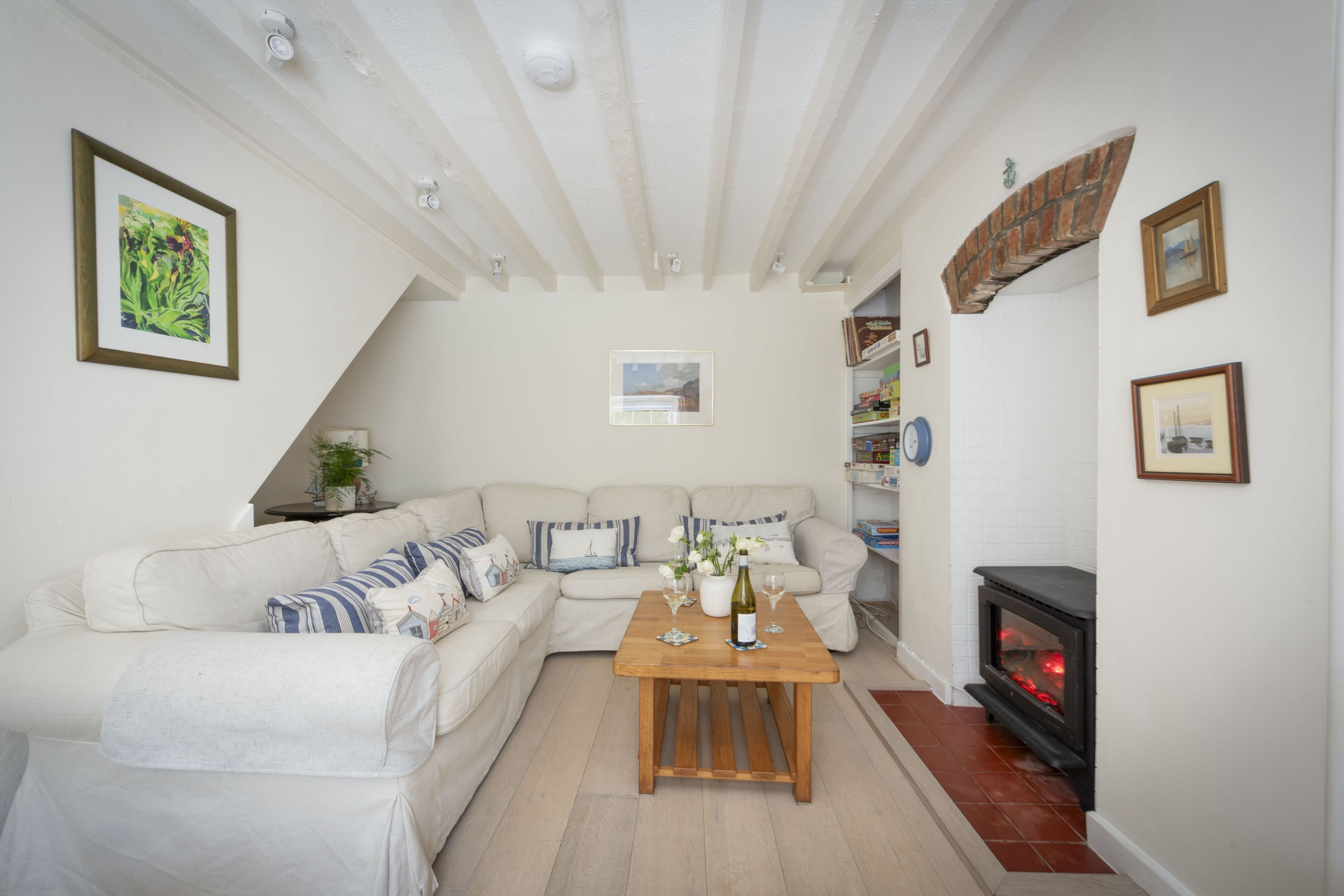 Una sala de estar acogedora con un sofá modular, una mesa de centro de madera, una chimenea y un techo blanco con vigas a la vista.