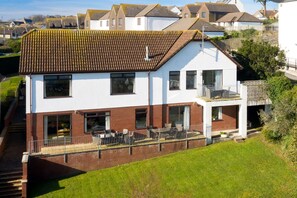 Ein zweistöckiges Haus mit Balkon, umzäunter Terrasse und Rasenfläche.