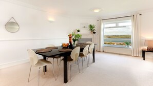 Un coin repas avec une table noire, des chaises de couleur beige et une vue sur la mer, visible à travers une grande fenêtre.