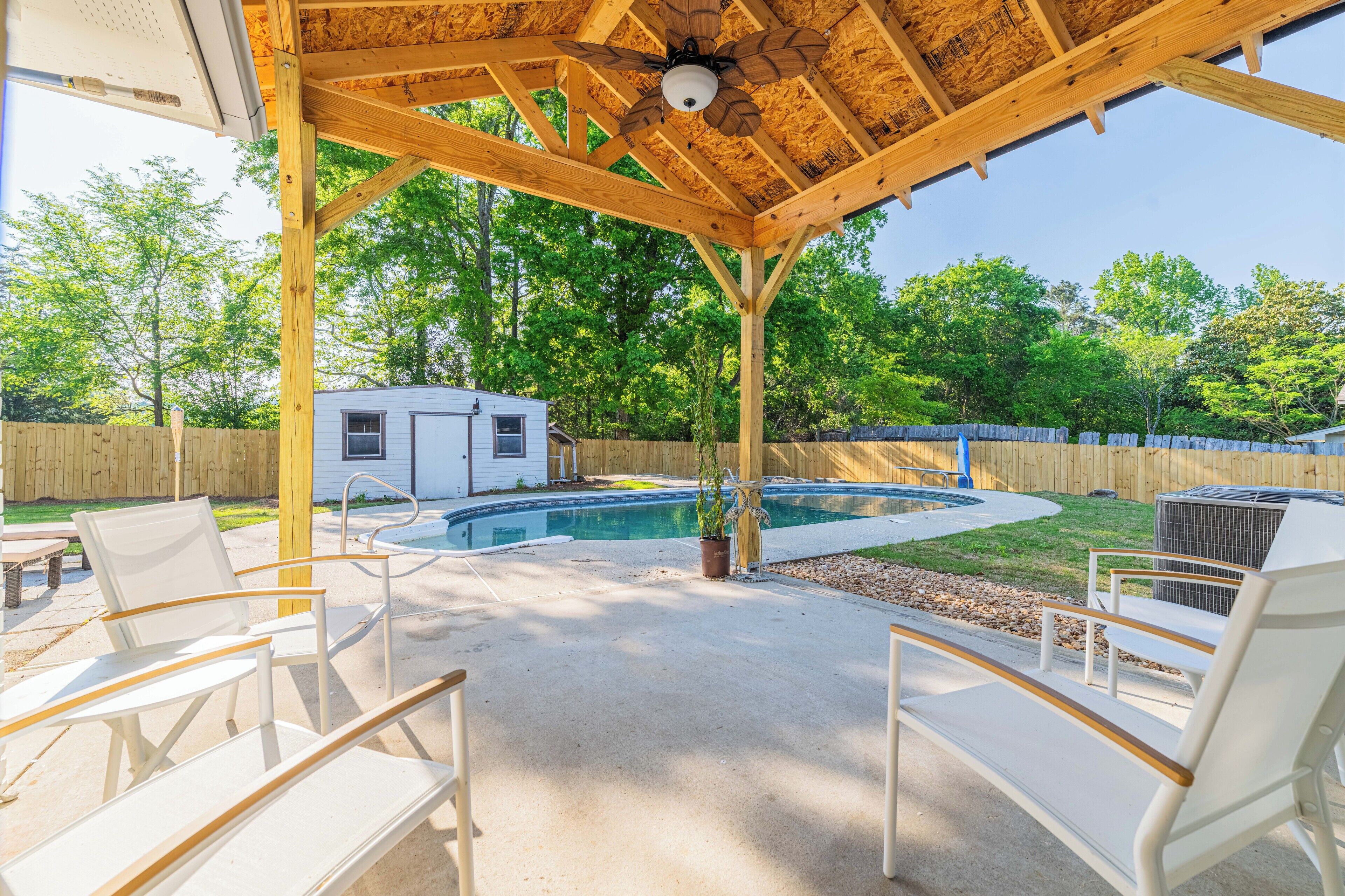 A covered patio with a pool, lounge chairs, and a small house in the background.