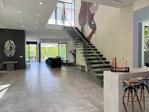 Un amplio salón con una escalera moderna, un ventanal grande y un diseño minimalista.