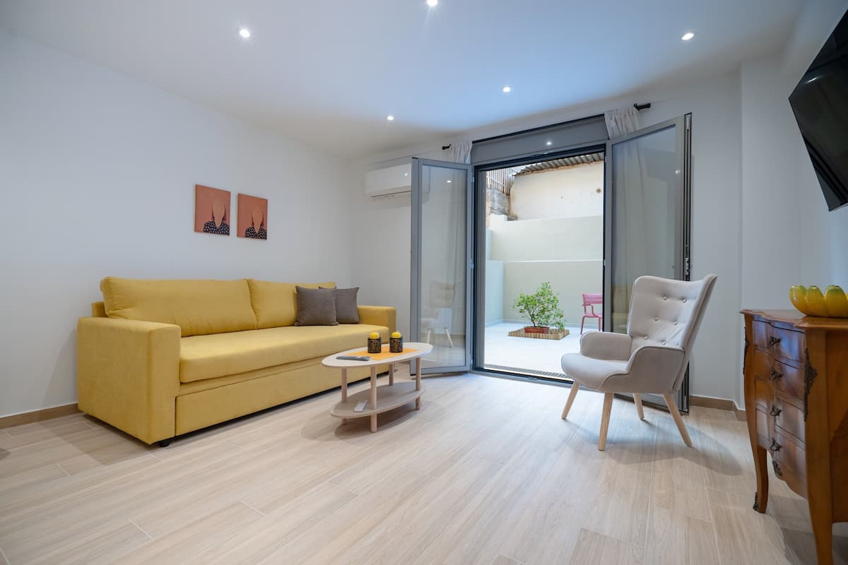 Uma sala de estar moderna com um sofá amarelo, uma poltrona branca, uma mesinha redonda e um armário de madeira.