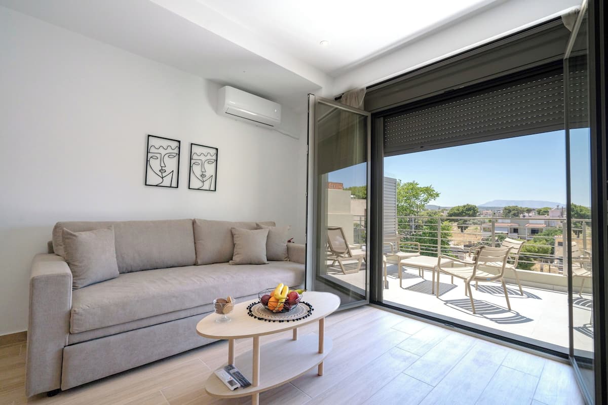 Uma sala de estar moderna com um sofá, uma mesa de centro com frutas e uma varanda com mobiliário de exterior.