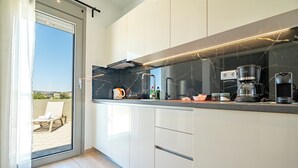 A modern kitchen with white cabinets, a black marble backsplash, and a coffee maker. - Arte 80 (Spata-Artemida)
