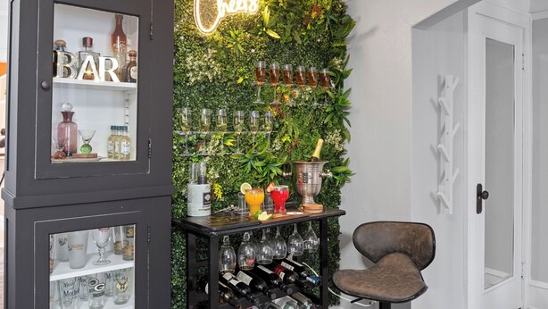 A bar area with a neon sign, a wine rack, and a bar cart.