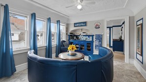 A modern living room with a blue sofa set, a round coffee table with a vase of sunflowers, and a blue cabinet with kitchen items.
