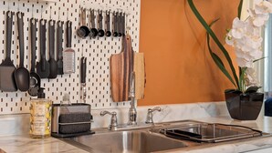 A kitchen with a marble countertop, white cabinets, and a pegboard with kitchen utensils.