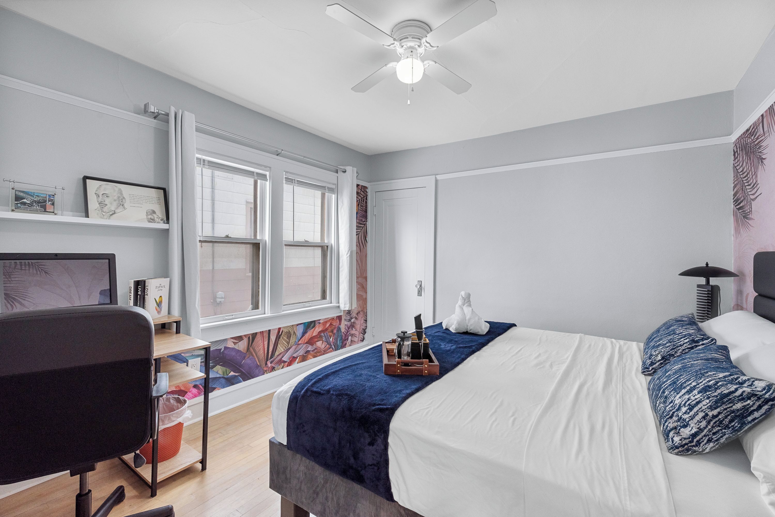 A bedroom with a bed, a desk, a chair, a ceiling fan, and a window with curtains.
