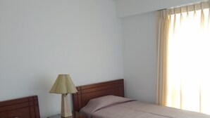 Ein Hotelzimmer mit zwei Einzelbetten, einem Nachttisch mit Lampe, einem Holz-Kopfteil und einem Fenster mit Vorhängen.