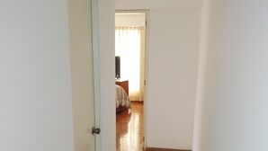 Ein schmaler Flur mit Holzboden, der zu einem Schlafzimmer mit Bett und Fernseher führt.