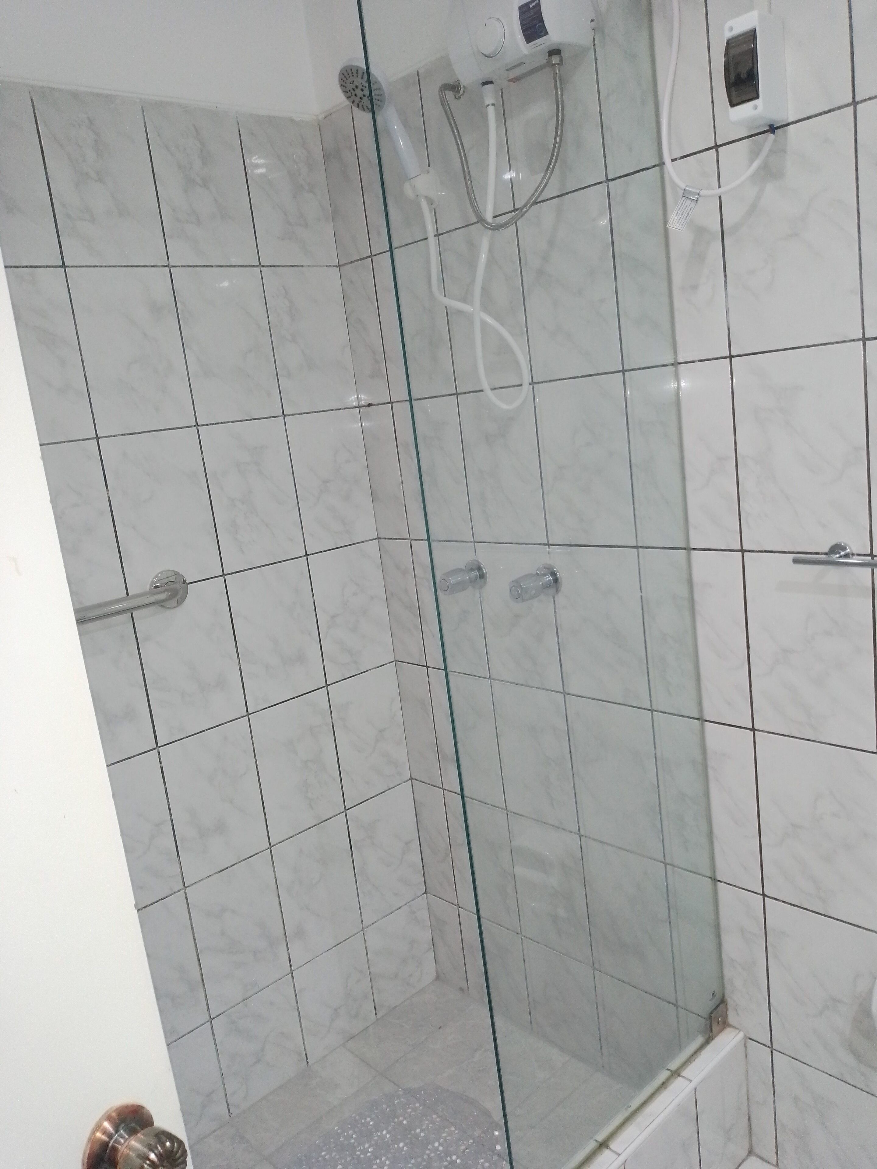 A bathroom with a glass shower enclosure, white marble tiles, and a visible shower control panel.