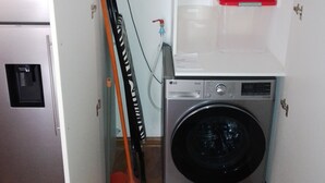 Eine kompakte Küche mit Waschmaschine, einer kleinen Ablage für Reinigungsmittel und einem an die Wand gelehnten Besen.