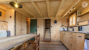 A wooden interior with a dining table and chairs, a kitchen with cabinets and appliances, and a staircase leading to another room. - Gîte - HAUTELUCE - Alpine chalet (HAUTELUCE)