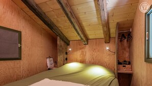 A cozy wooden room with a bed, a small shelf with items, and a wall-mounted light fixture. - Gîte - HAUTELUCE - Alpine chalet (HAUTELUCE)