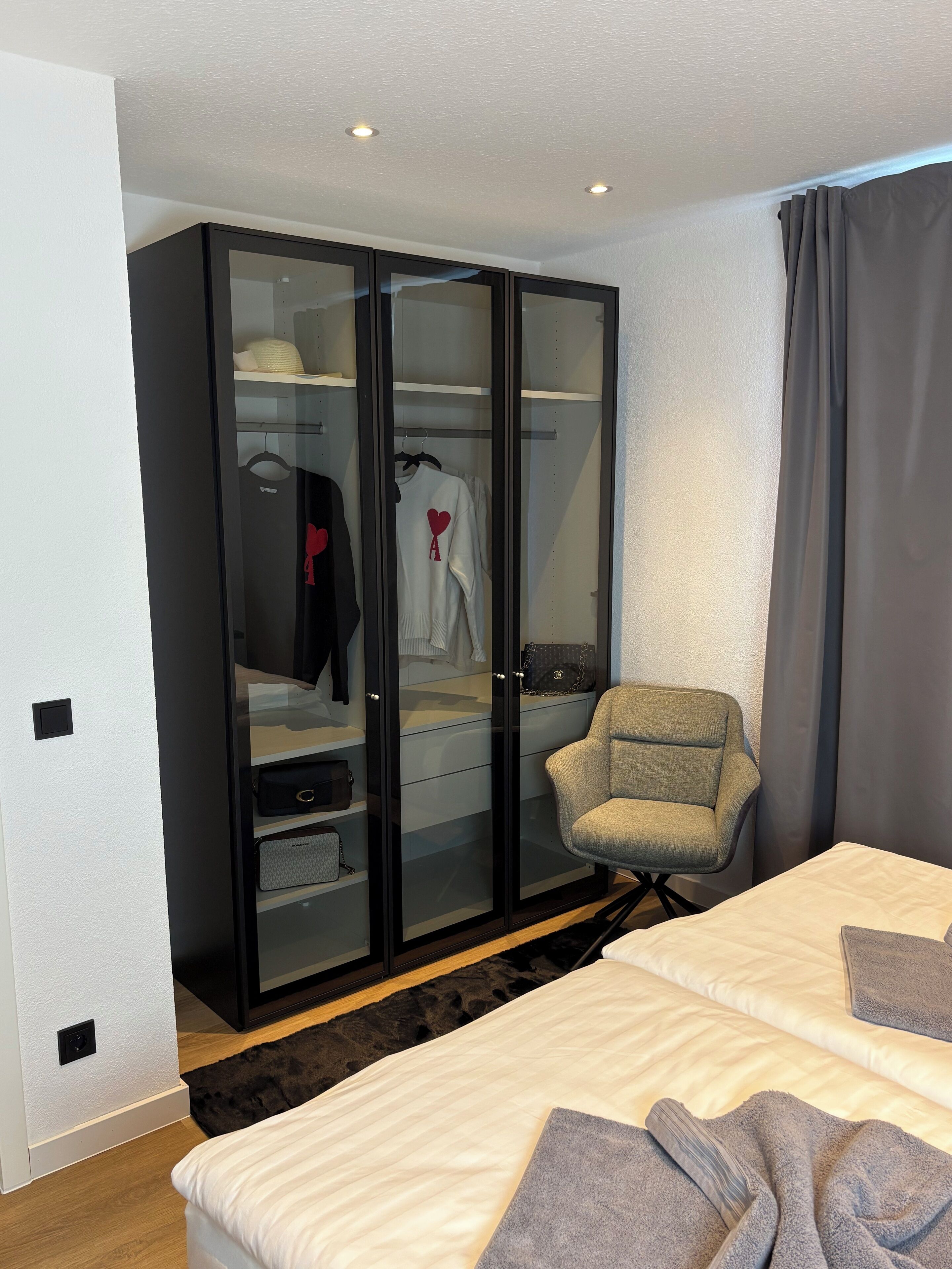 Een hotelkamer met een grote garderobe, een grijze fauteuil en een bed met een grijze deken.