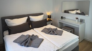 Un dormitorio moderno con una cama grande, mesitas de noche, un escritorio y un espejo.
