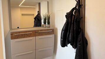 A modern hallway with a wooden floor, a white cabinet with drawers, a mirror, and a coat rack with jackets.